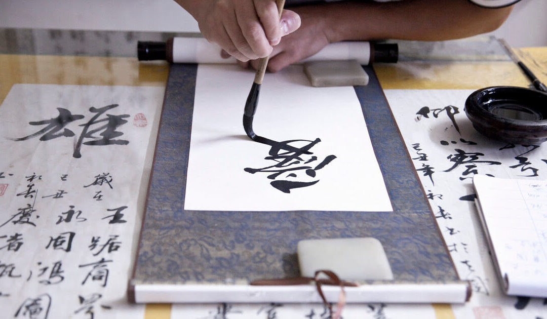manos de un calígrafo haciendo símbolos de caligrafía japonesa con pincel y tinta sobre papel
