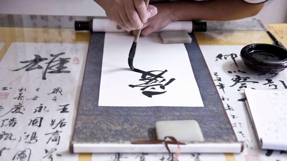 arte-shodo-caligrafía-japonesa manos de un calígrafo haciendo símbolos de caligrafía japonesa con pincel y tinta sobre papel